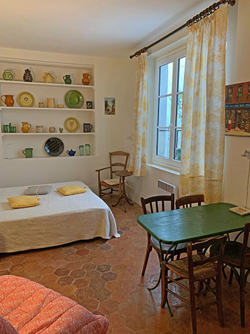 View of studio misc. pottery, queen bed, through cushions, armchair and small oval table, dining table, bistro chairs.